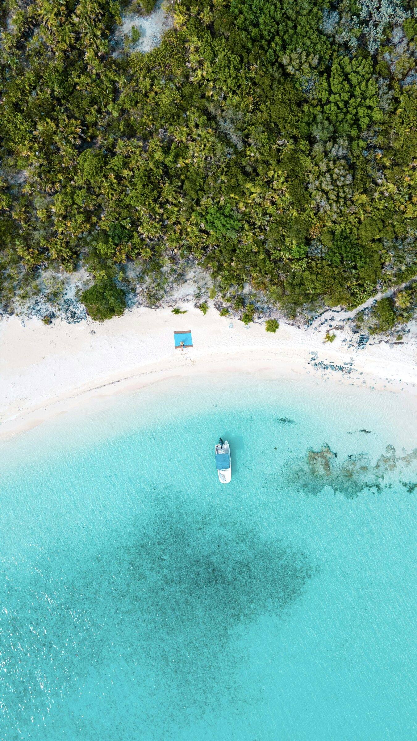 Aerial view of a small boat at anchor off a white-sand beach in clear turquoise water