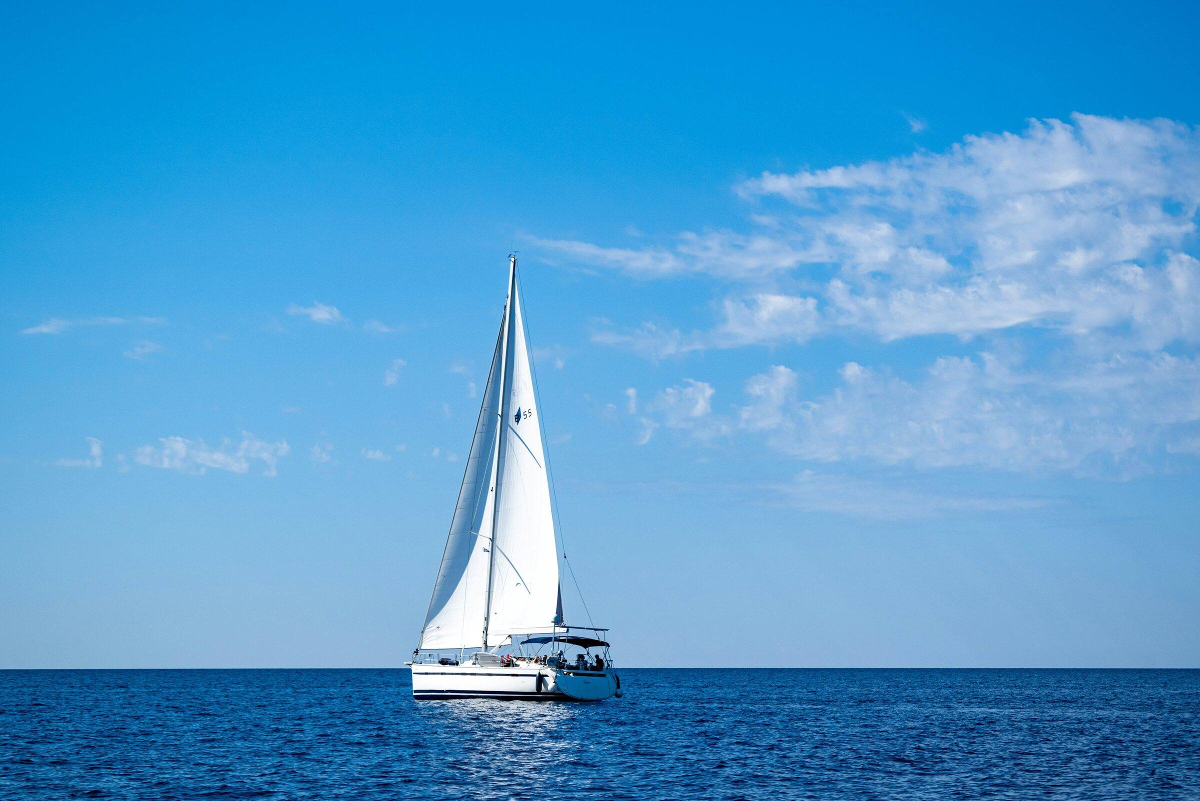 White sailing yacht under sail on deep blue sea beneath a blue sky with light clouds
