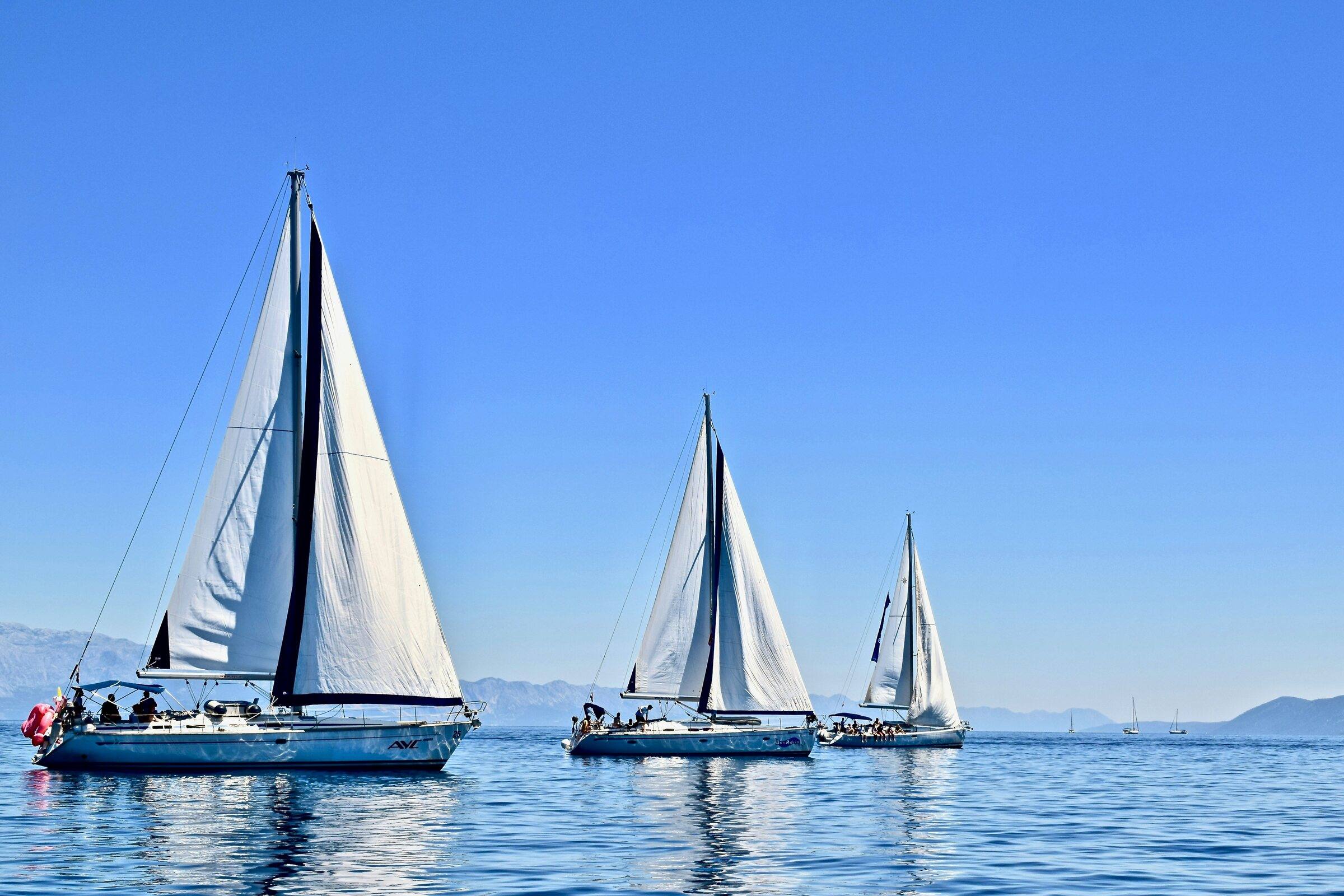 Three sailing yachts under sail on calm blue water with a distant coastline