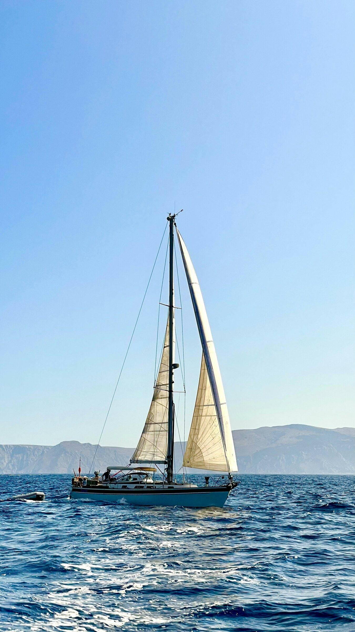 Sailing yacht under sail on deep blue sea with hazy mountains behind