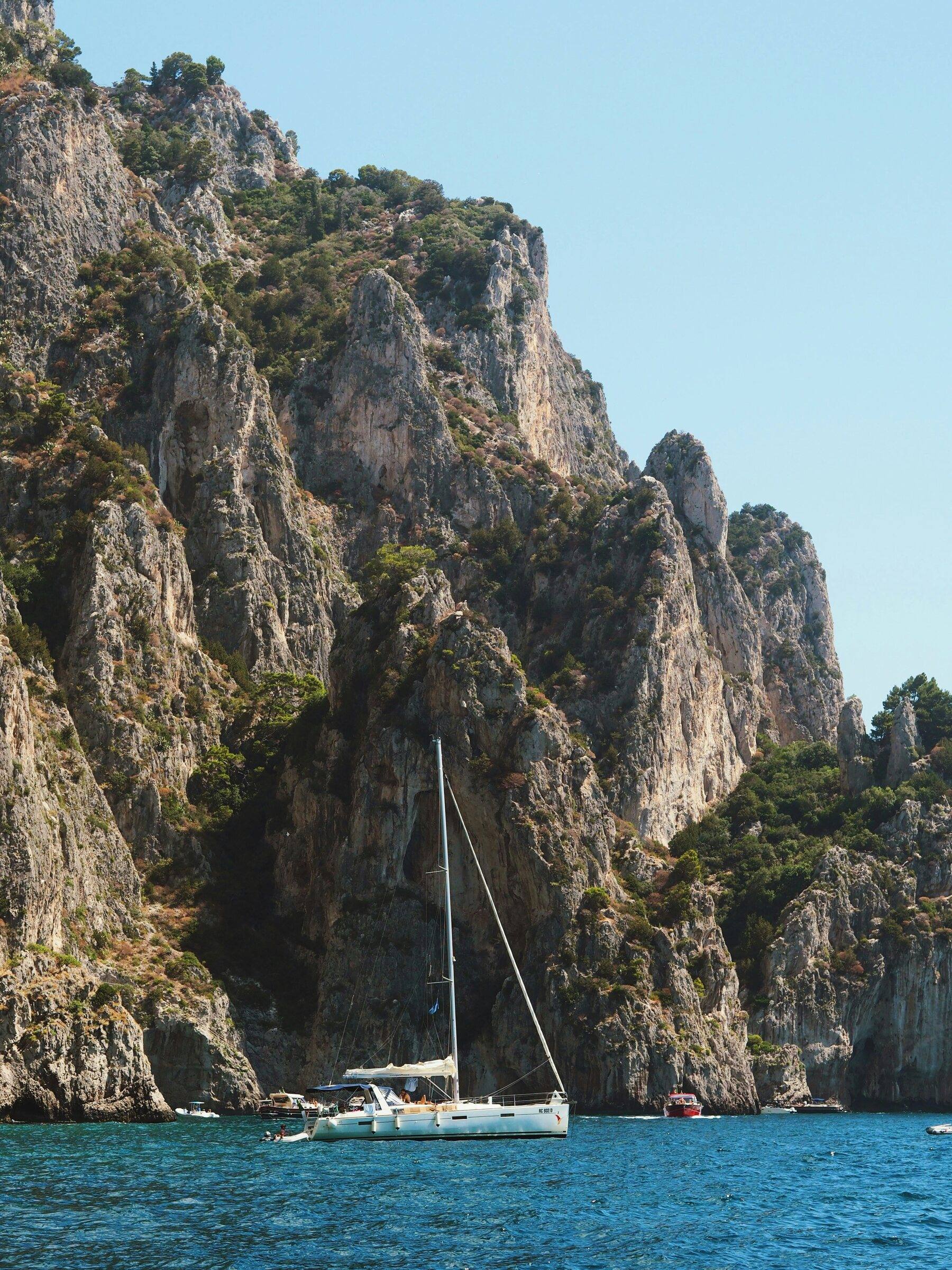 Sailing yacht at anchor at the foot of steep, rocky cliffs on the sea