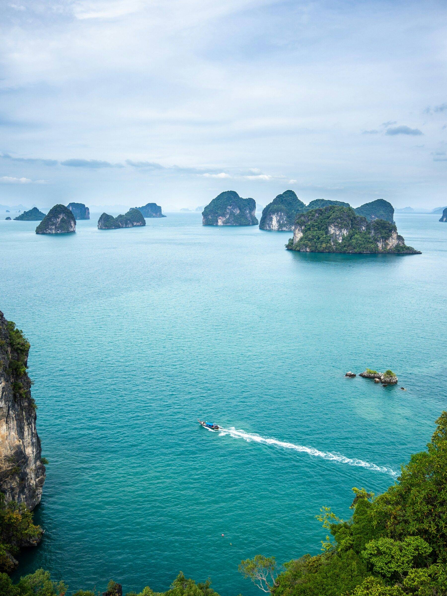 Limestone islands rising from turquoise sea, with a small boat leaving a wake in the distance